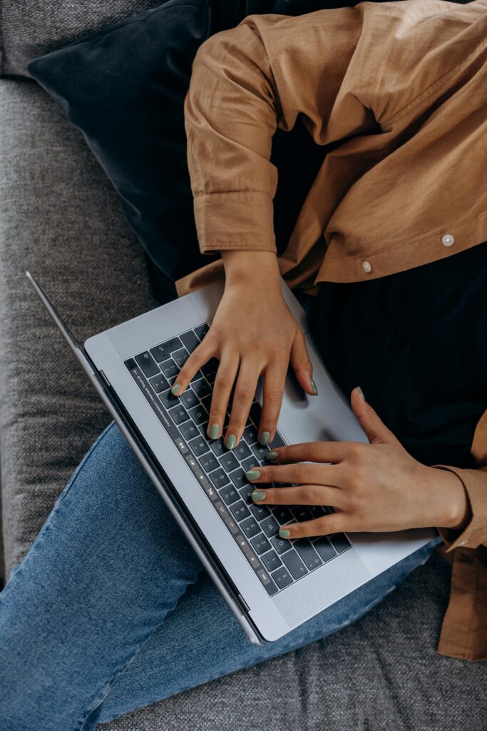 pexels-photo-6893955-6893955 A person typing on a laptop while seated on a couch with casual attire, perfect for remote work imagery.